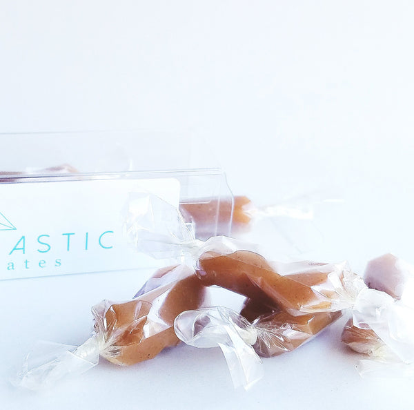 Apple Cider Caramels sit haphazardly in front of their open box on a white background.